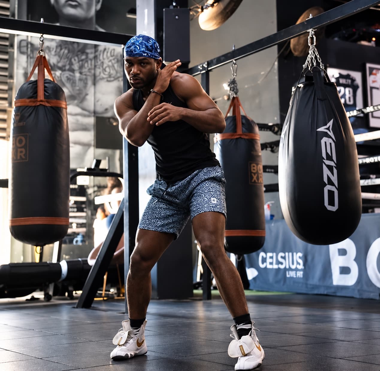 Kenneth Sene in a blue durag shadowboxing between heavy bags in a boxing gym