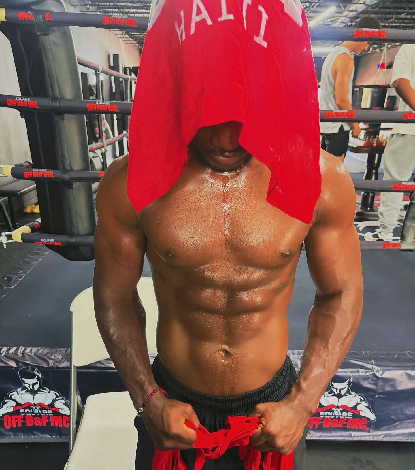 Kenneth Sene shirtless in the gym with a red Haiti shirt pulled over his head